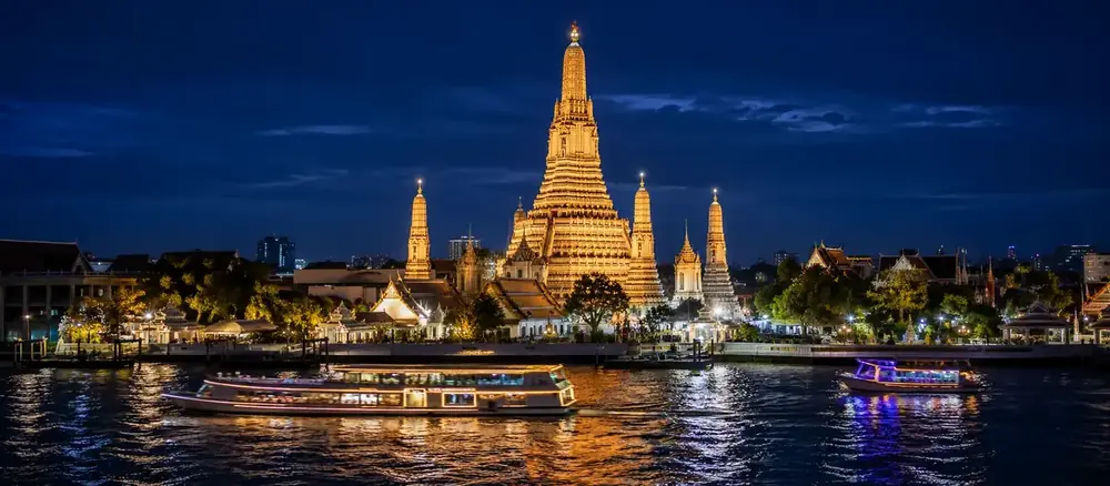 Wat Arun lit up at night with dinner cruise boats on the Chao Phraya river, Bangkok